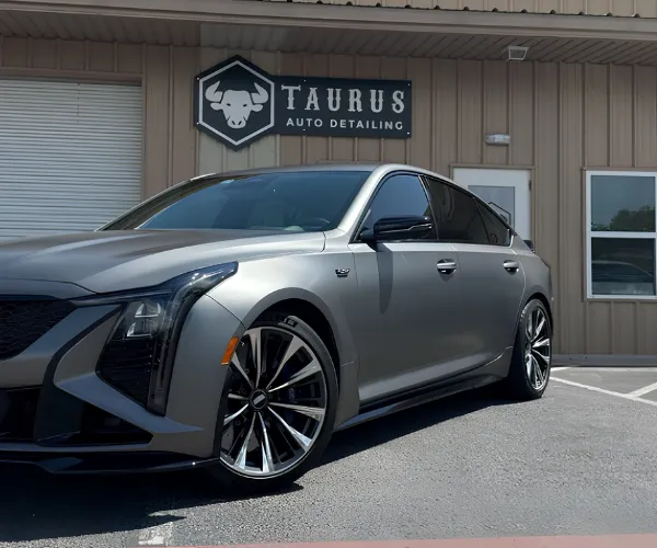 view of a black sports car parked inside a brightly lit detailing garage, showcasing a high-gloss, reflective ceramic coating finish on the hood and body.