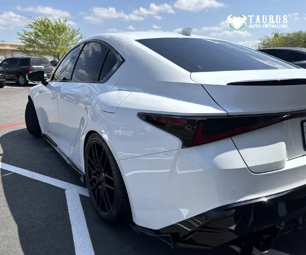 A rear three-quarter view of a white performance sedan featuring a black rear spoiler, tinted taillights, and a black rear diffuser.