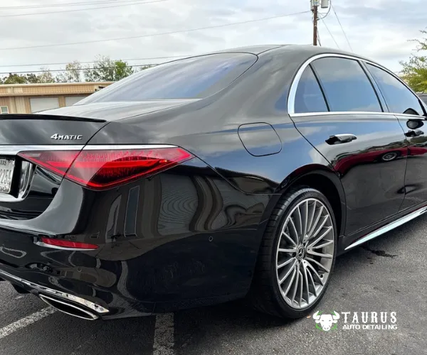 A front three-quarter view of a glossy black luxury Mercedes-Benz sedan parked in front of a shop featuring the Taurus Auto Detailing sign