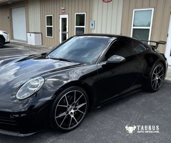 view of a glossy black Porsche coupe with dark tinted windows parked outside