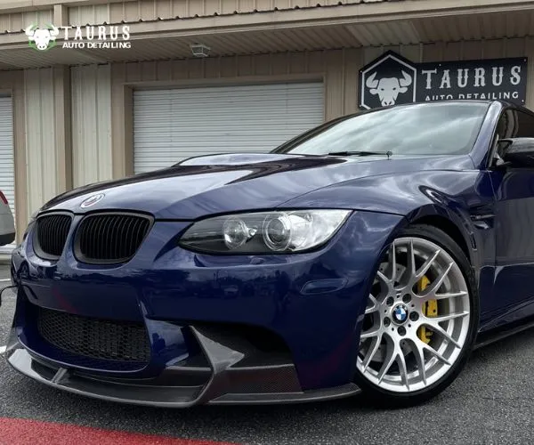 Close-up front-left view of a dark blue BMW M3 highlighting the front bumper, headlight, and silver alloy wheel.